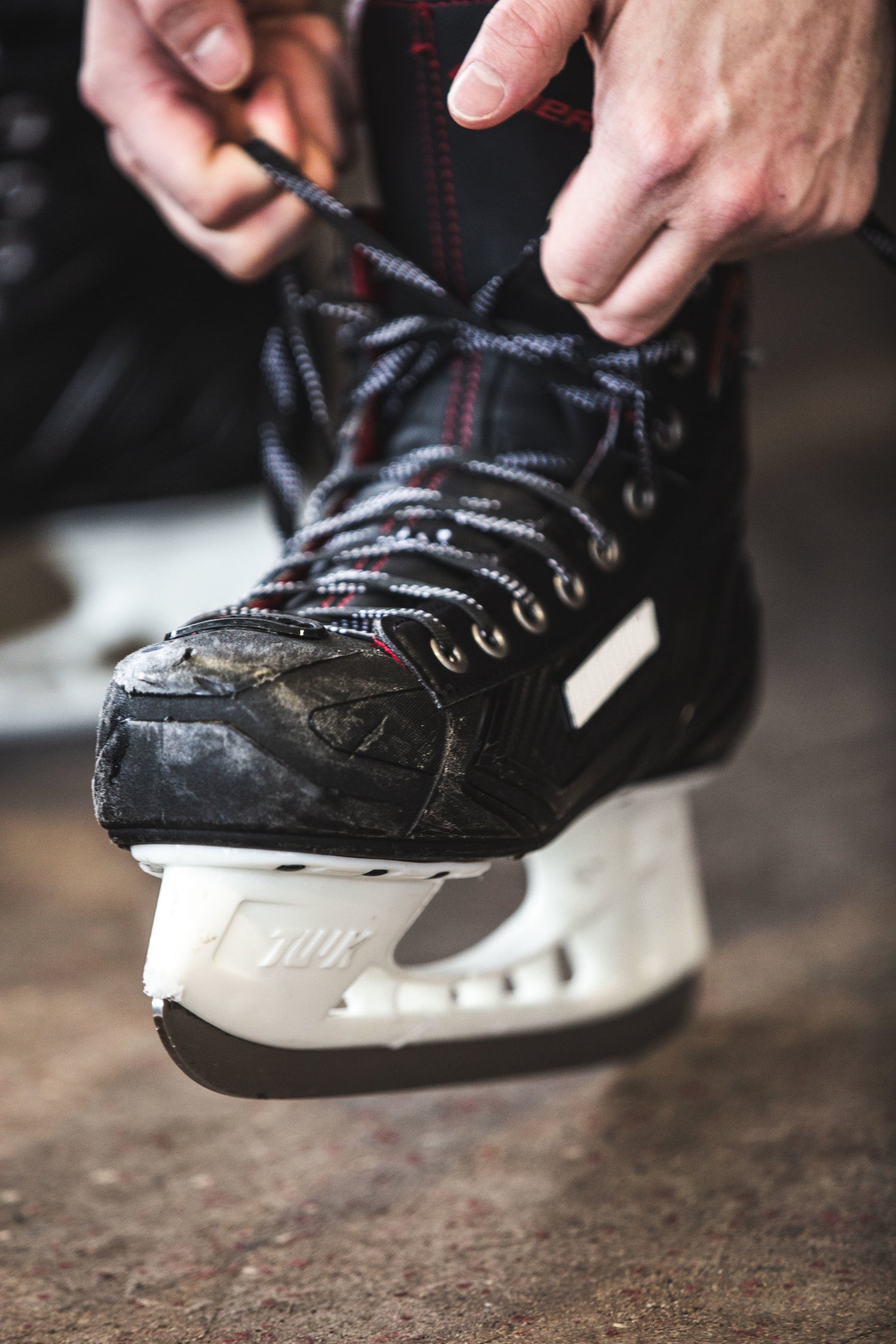 A pair of hands ties the laces of a black, worn hockey skate.
